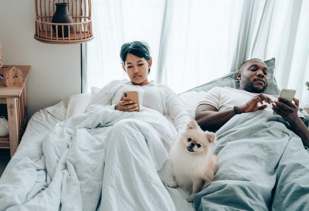 multiracial couple surfing mobile phones lying in bed with 4545196